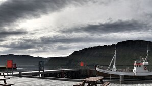 A dock with a boat, wooden benches, and a mountainous backdrop. - Hildibrand Hotel (Fjardabyggd)