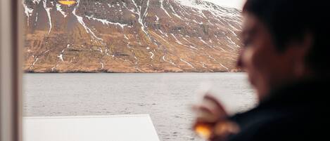 A person holding a glass, with a mountain and a building in the background.
