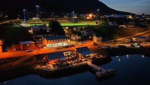 A waterfront property with a dock, a building with multiple rooms, and a sports field in the background. - Hildibrand Hotel (Fjardabyggd)