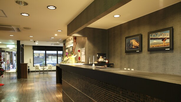 A reception area with a counter, chairs, and framed pictures on the wall. - Business Hotel SUNP (Shizuoka)