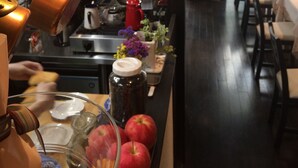 A kitchen area with hanging copper pots, a coffee machine, and a variety of fruits and flowers on the counter. - Business Hotel SUNP (Shizuoka)