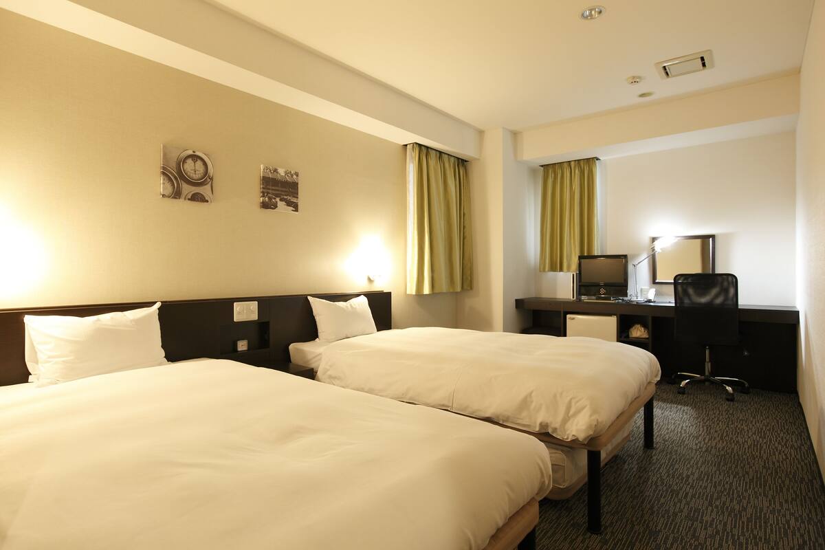 A hotel room with two beds, a desk, a chair, and a television.
