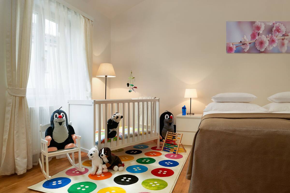 A baby room with a crib, a colorful play mat, a white chair, and plush toys.