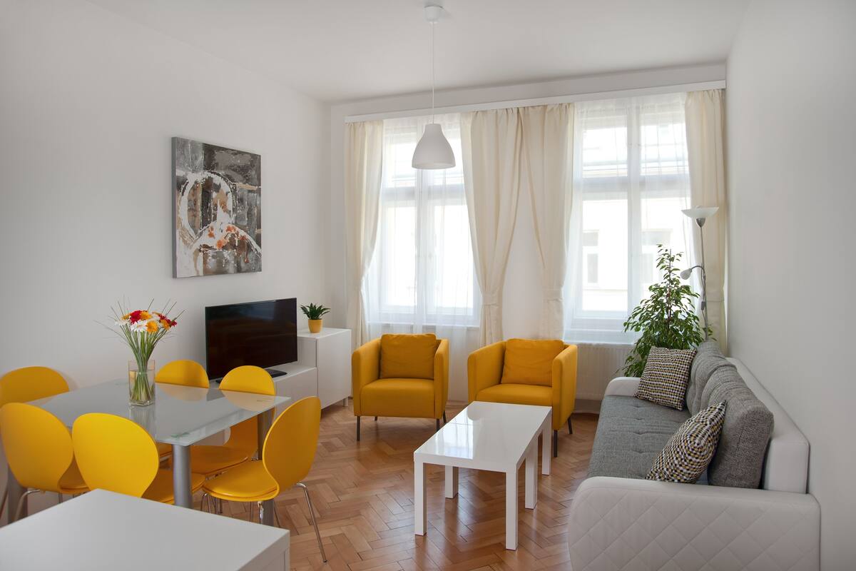 A modern living room with a sofa, two yellow armchairs, a white coffee table, and a dining area with a table and chairs.