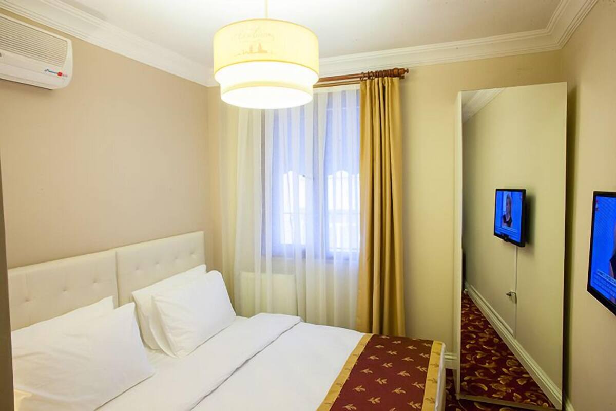A hotel room with a bed, a television on the wall, and a window with curtains.