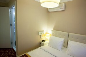 Ein Hotelzimmer mit Bett, Nachttischlampe, Nachtschränkchen und einer Klimaanlage an der Wand.
