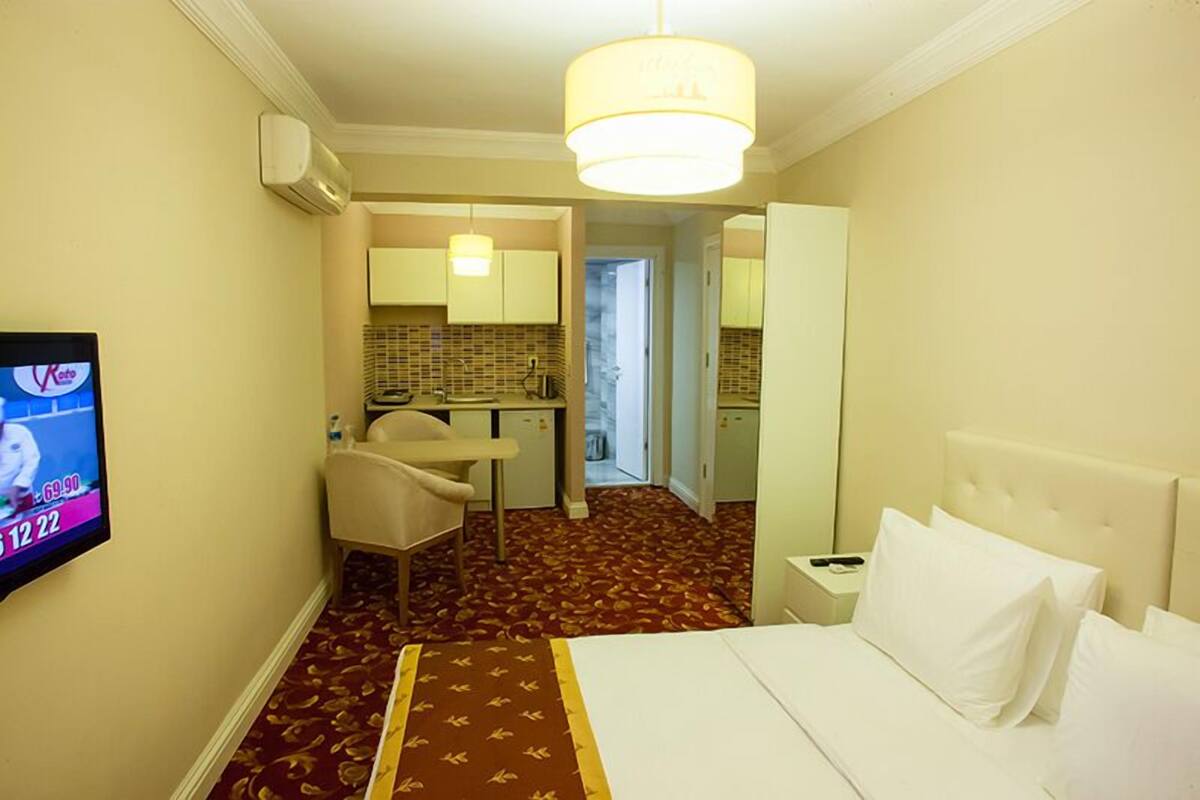 A hotel room with a bed, a desk, a chair, a television, and a kitchenette.