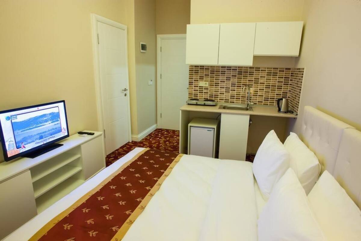 A hotel room with a bed, a television, a kitchenette, and a bathroom.
