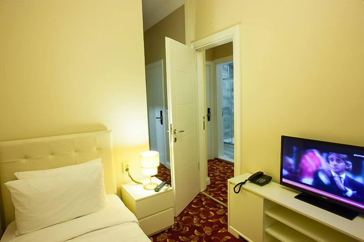 A hotel room with a bed, a bedside lamp, a television, and a telephone.