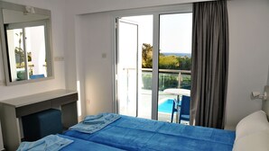 Une chambre d’hôtel comprenant un lit, un bureau, une chaise, une fenêtre donnant sur une piscine et sur de la verdure, ainsi qu’un balcon.