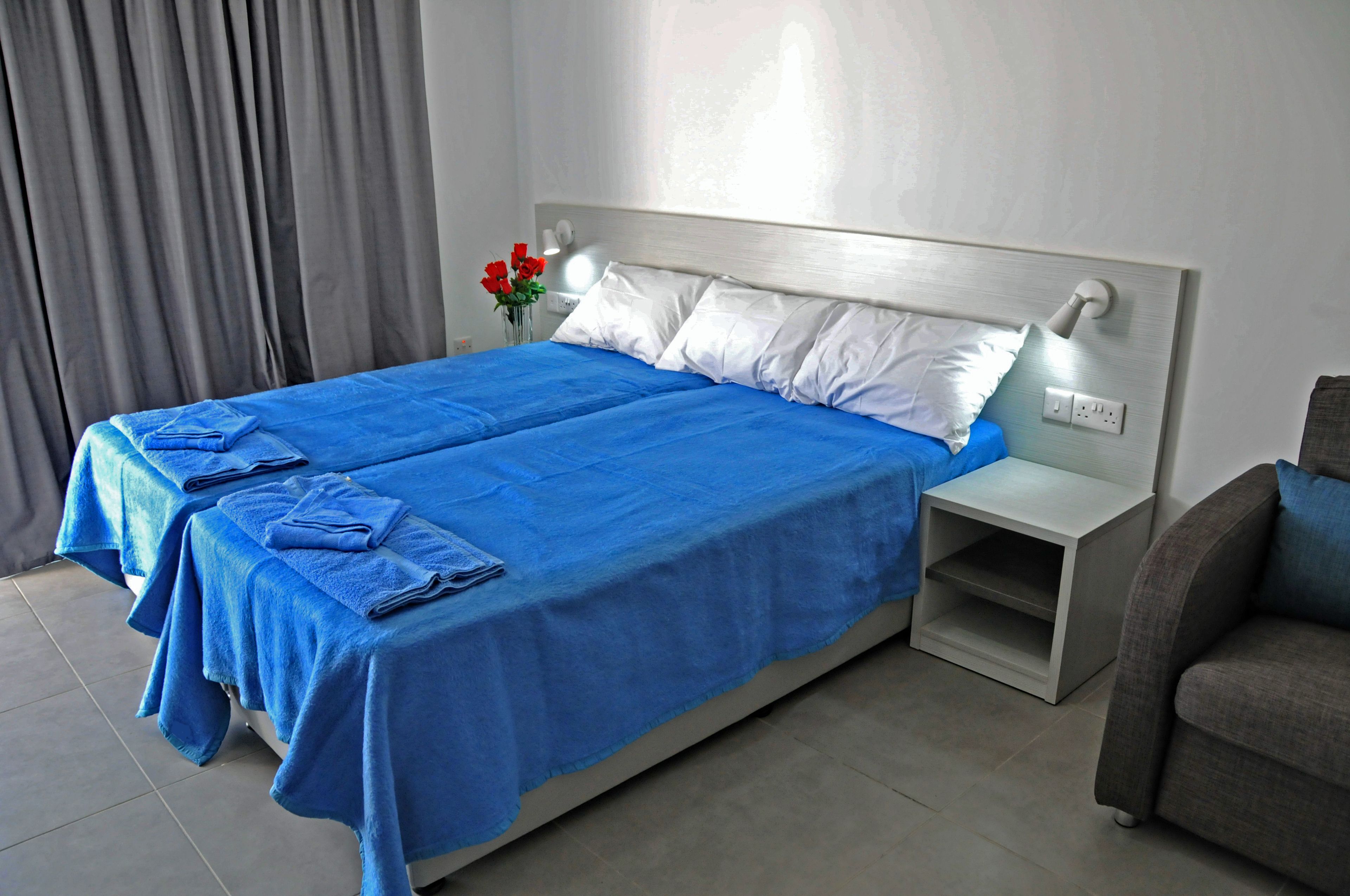A hotel room with a large bed, two pillows, a nightstand, and a vase with flowers.