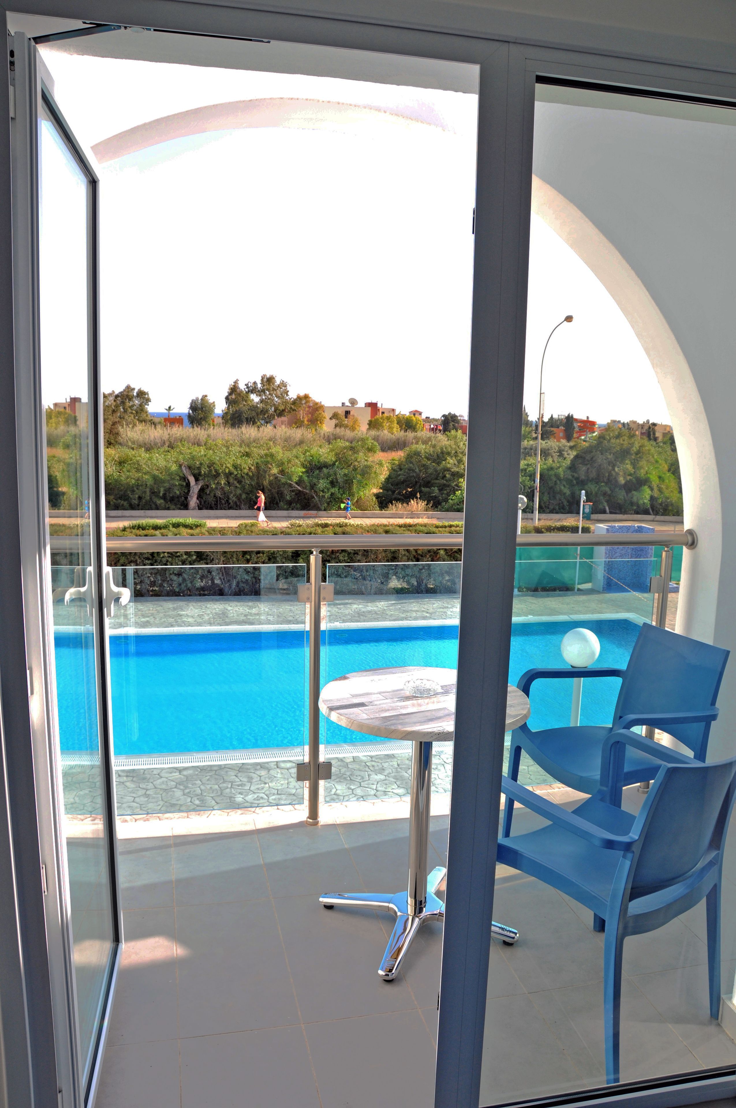 Un balcón con puerta de vidrio, piscina y mesa con sillas.