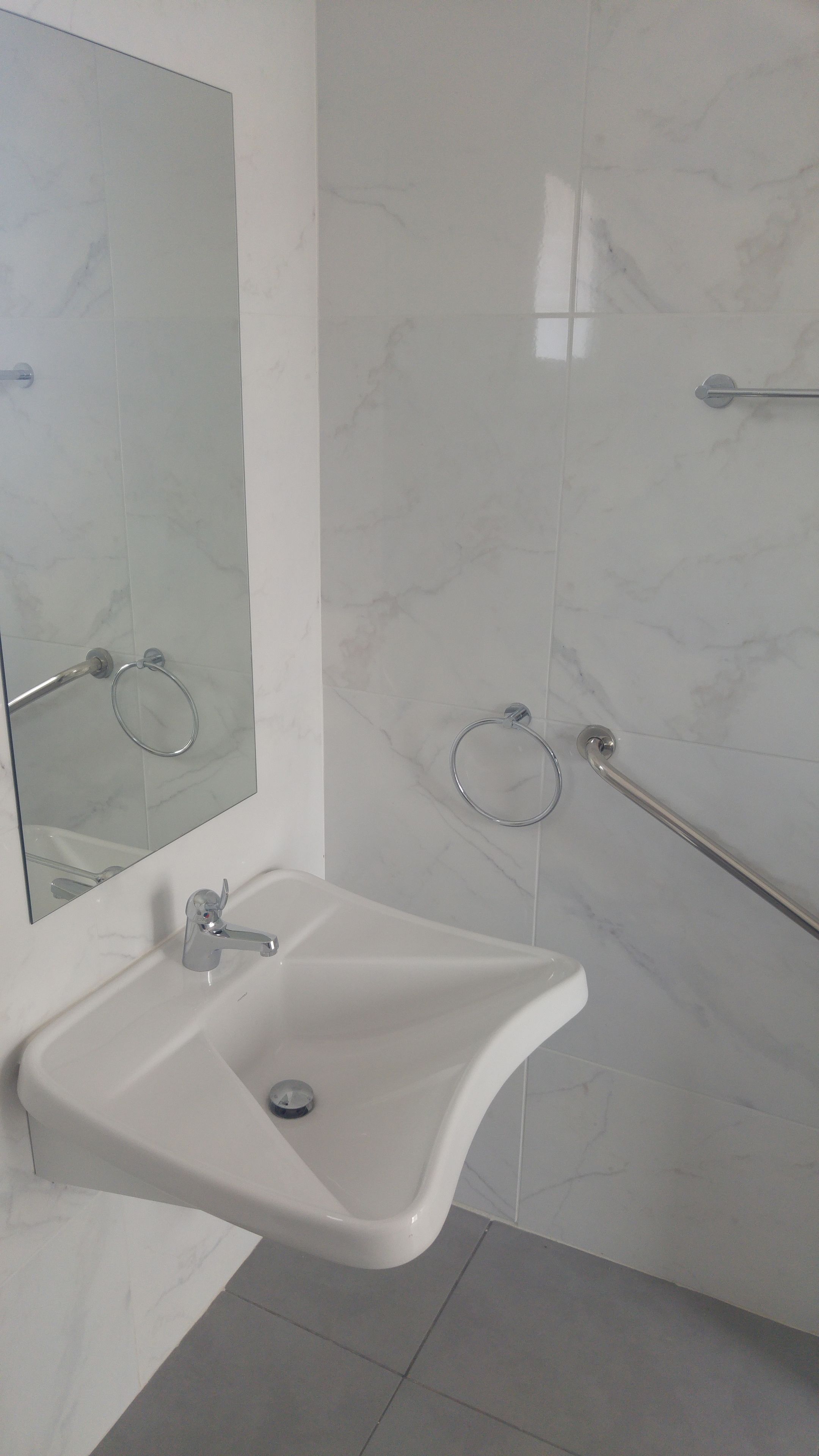Ein Badezimmer mit einem weißen Waschbecken, einem Spiegel und einem Handtuchhalter.