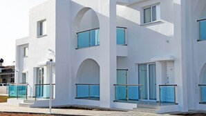 Un bâtiment moderne aux murs extérieurs blancs, doté de grandes fenêtres en arc de cercle et de balcons avec des garde-corps en verre.
