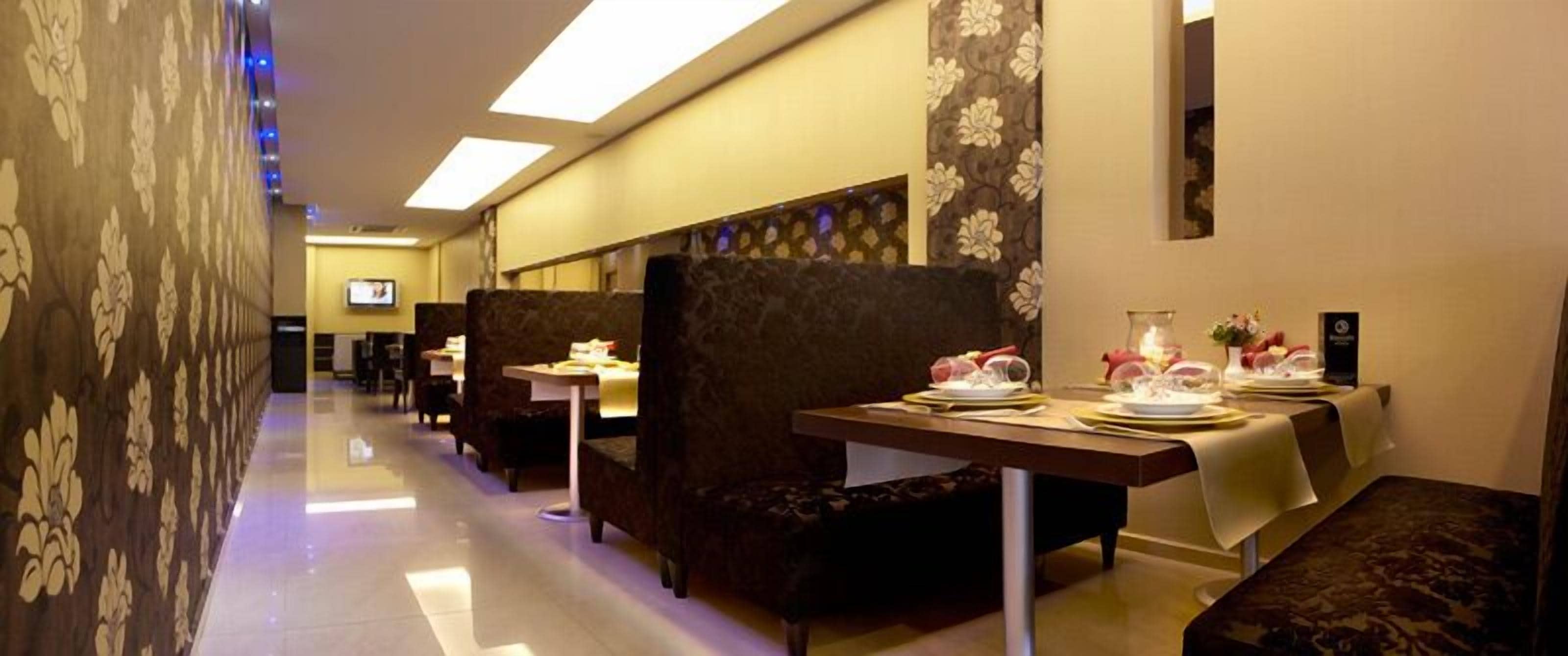 A hotel corridor with seating areas, tables set for dining, and a television screen.