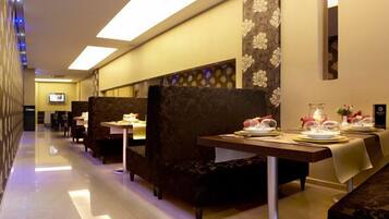 A hotel corridor with seating areas, tables set for dining, and a television screen.