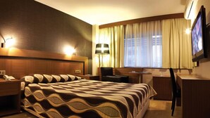 A hotel room with a large bed, a desk, a chair, a TV, and a window with curtains. - Susuzlu Hotel (Izmir)