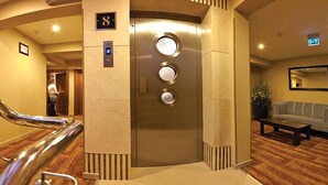 A hotel lobby with a modern elevator, a staircase, and a seating area with a sofa and coffee table. - Susuzlu Hotel (Izmir)