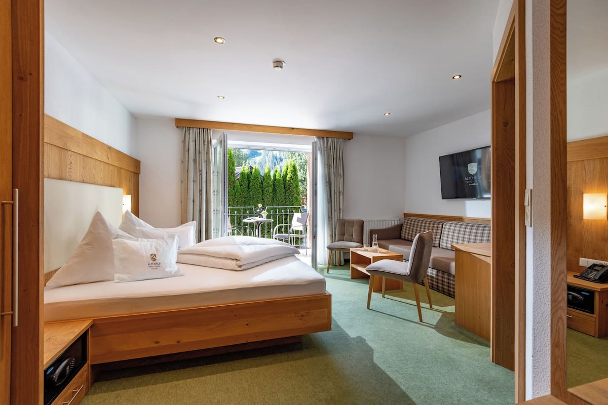Une chambre d’hôtel avec un lit, un bureau, une chaise et une vue sur la verdure environnante.