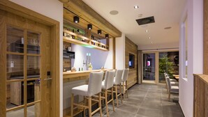 Een moderne bar met houten details, barstoelen en een glazen vitrine.