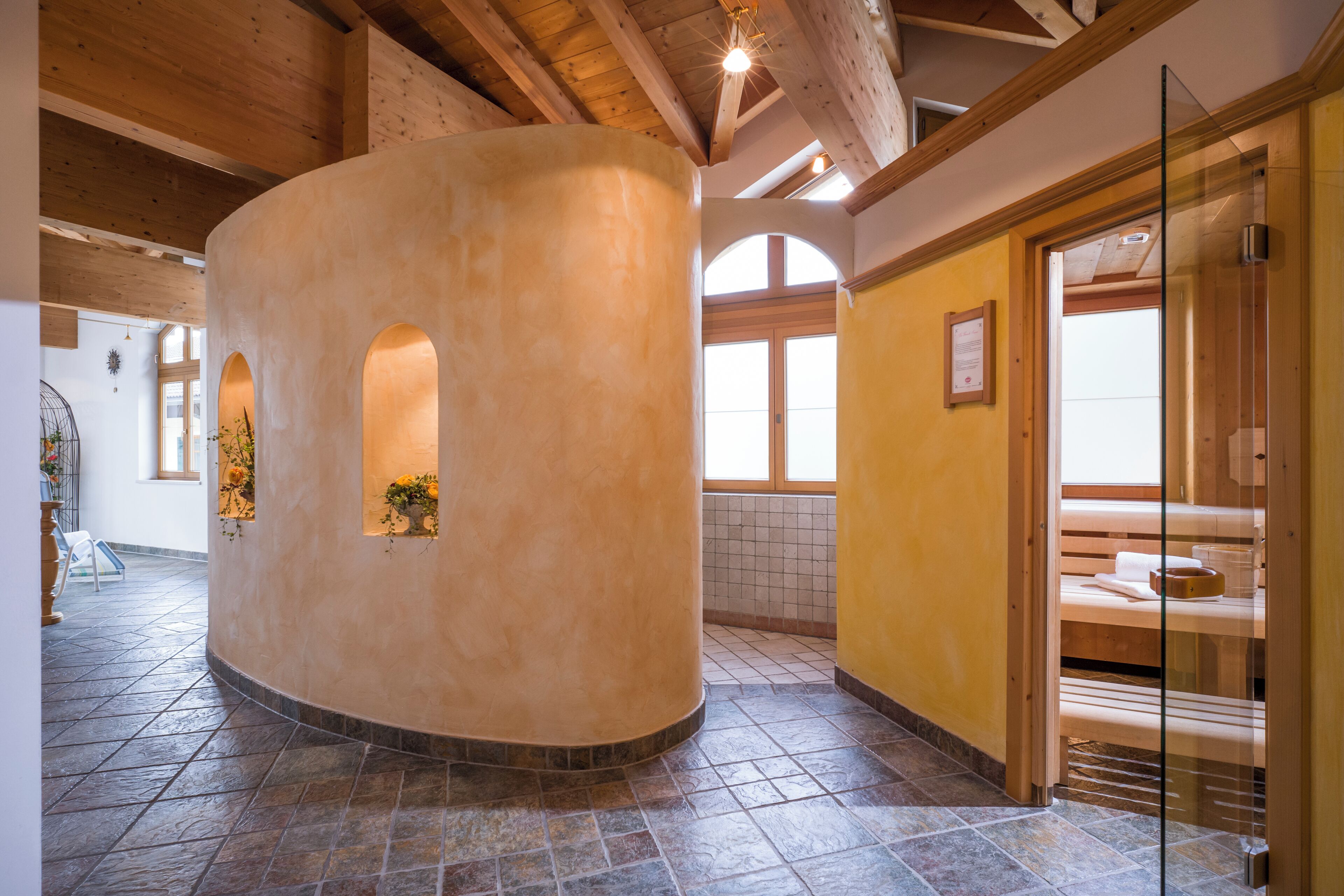 A spa area with a curved wall, wooden beams, and a glass shower enclosure.