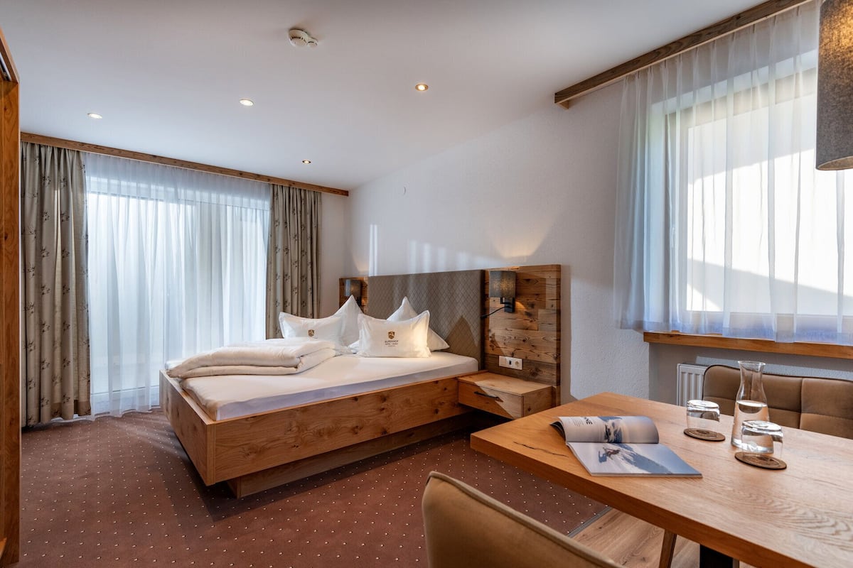 Une chambre d’hôtel comprenant un lit, un bureau, une chaise, une fenêtre avec des rideaux légers et un radiateur.