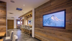 Een modern interieur met houten lambrisering, een groot scherm waarop een berglandschap te zien is, en een zithoek met stoelen en tafels.
