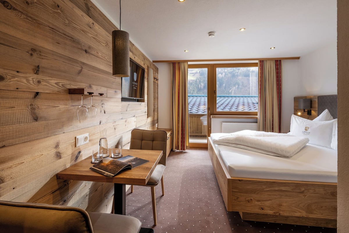Une chambre d’hôtel avec un mur en bois, un lit, un bureau avec une chaise et une fenêtre avec des rideaux.