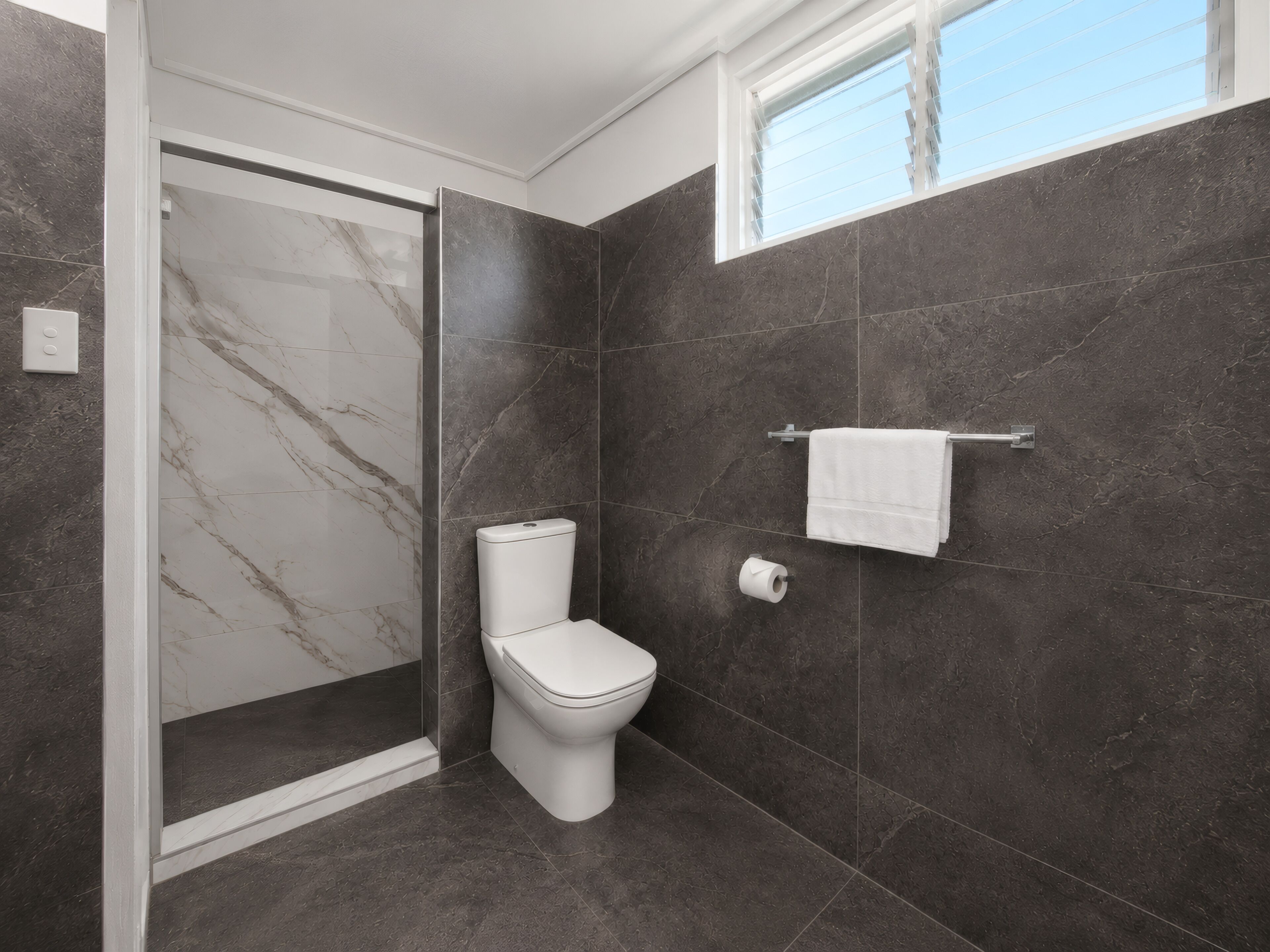 Une salle de bain moderne équipée de toilettes, d’une douche et d’un porte-serviettes.