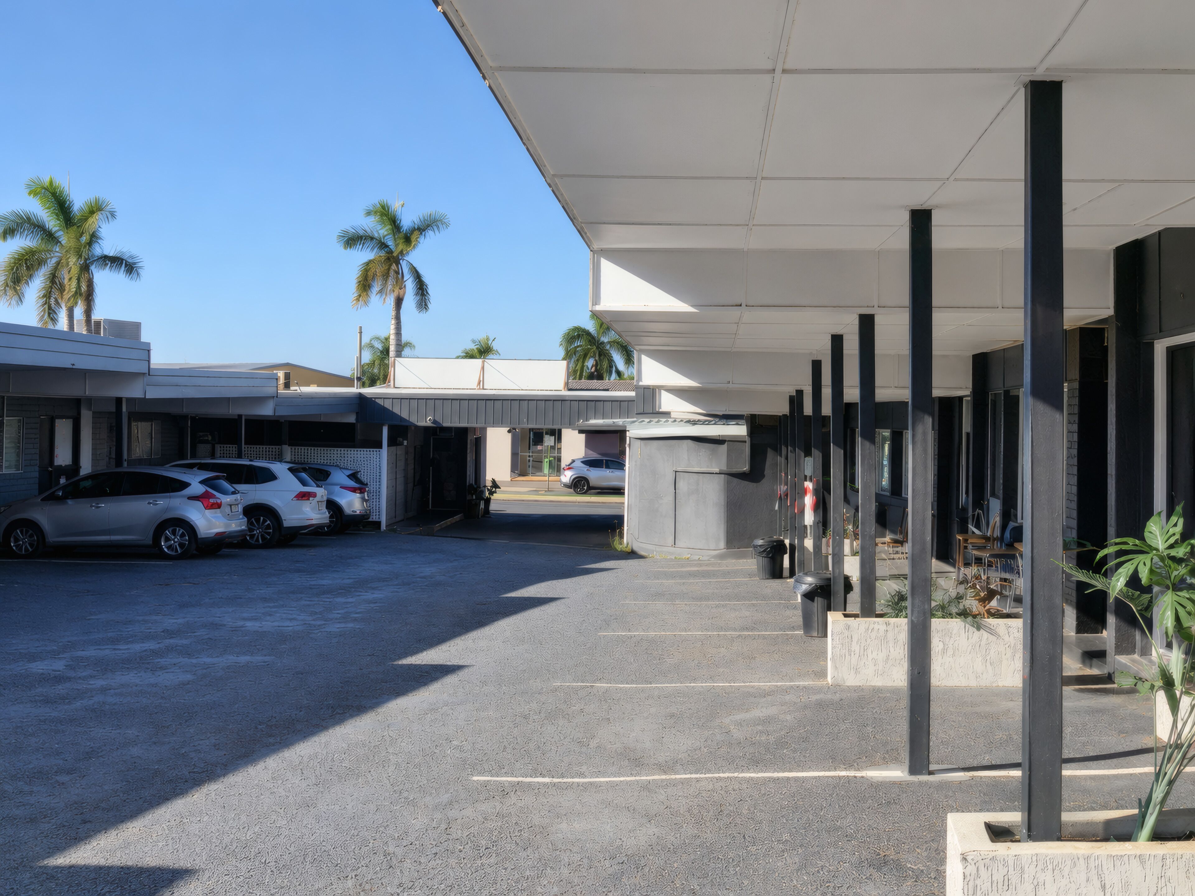 Un estacionamiento techado con una fila de columnas, entrada a un edificio y automóviles estacionados.