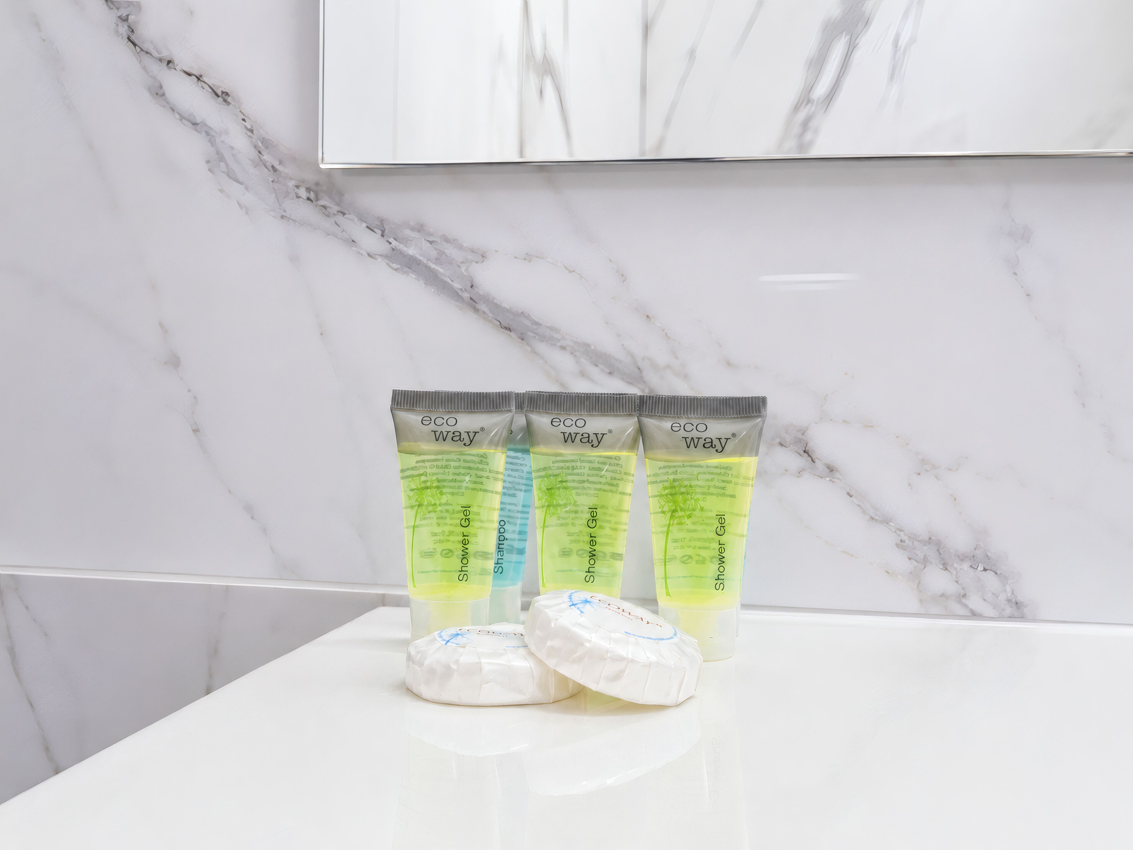 Tres tubos de gel de ducha ecológico y dos pastillas de jabón blancas sobre una encimera de mármol blanco.