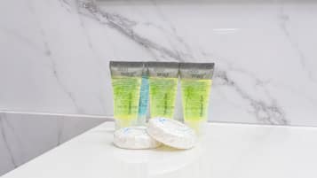 Tres tubos de gel de ducha ecológico y dos pastillas de jabón blancas sobre una encimera de mármol blanco.