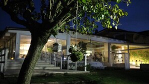 A modern house with a well-lit entrance, a tree in the foreground, and hanging planters. - La Pampa Relais (Melizzano)