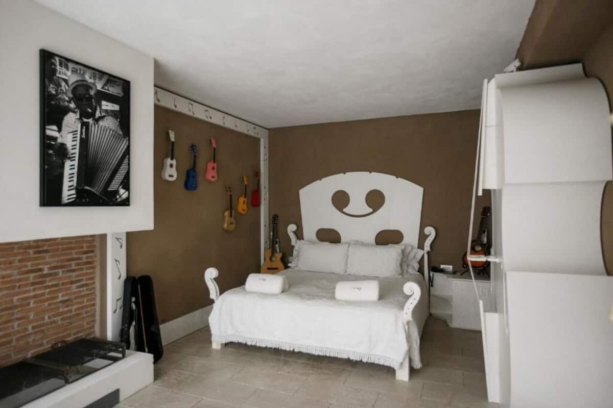 Un dormitorio con una cama blanca, una chimenea de ladrillo y guitarras colgadas en la pared.