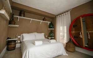 Une chambre à coucher avec un lit, un miroir rond, des étagères ornées d’objets décoratifs et une porte en bois.