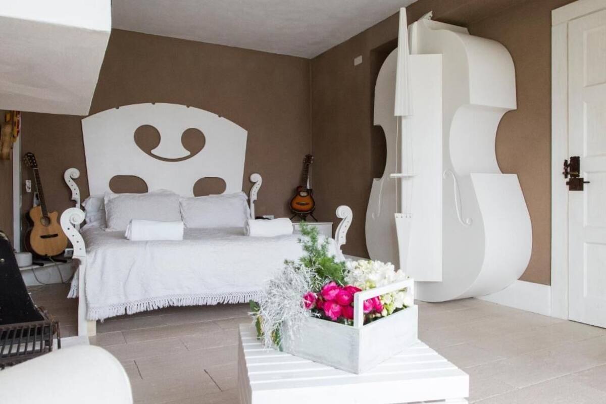 Un dormitorio con un diseño de cama original, una guitarra y un arreglo floral decorativo.