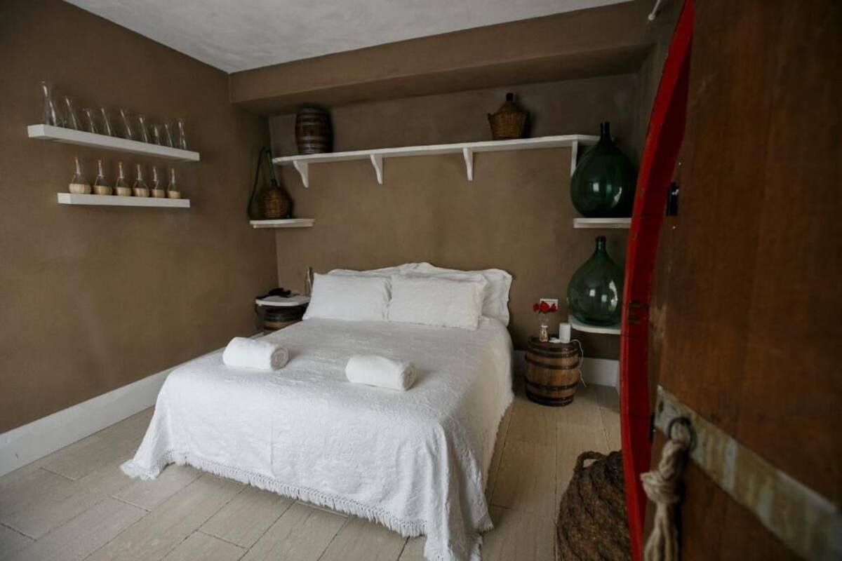 Un dormitorio con una cama grande, ropa de cama blanca, una mesita de noche de madera y estantes con objetos decorativos.
