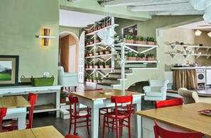 Un intérieur moderne avec un coin repas comprenant des chaises rouges et une table en bois, un escalier agrémenté de plantes en pot et un espace cuisine avec des étagères.