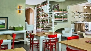 A modern interior with a dining area featuring red chairs and a wooden table, a staircase with potted plants, and a kitchen area with shelves. - La Pampa Relais (Melizzano)