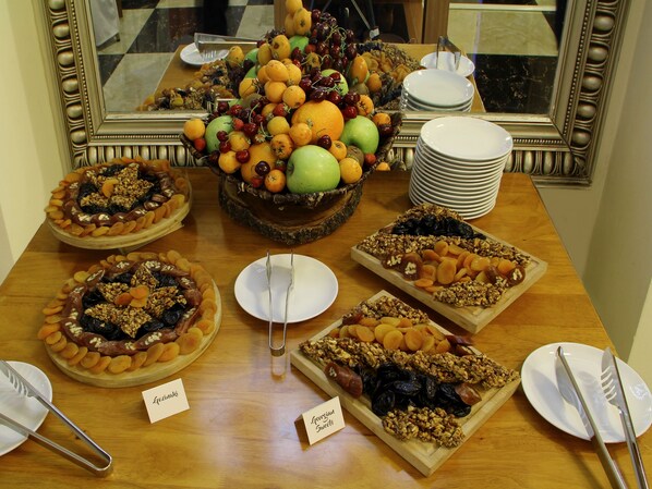 Une table de buffet avec différents plateaux de fruits et de fruits secs, des assiettes et des couverts.