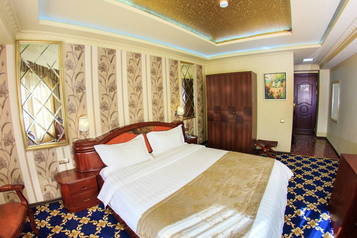 A hotel room with a large bed, a wooden wardrobe, a mirror, and a door.