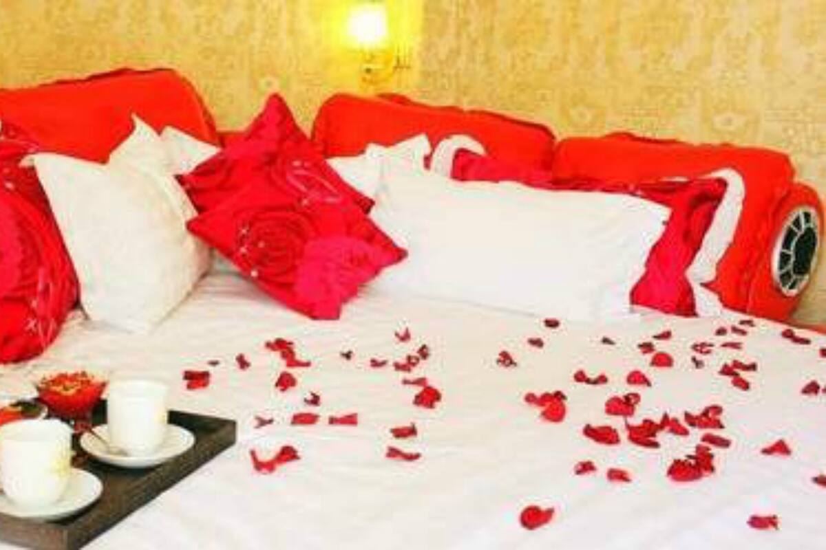 A bed with red and white bedding, a tray with cups and a flower, and rose petals scattered on the bed.