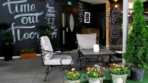 A lounge area with a black wall featuring motivational phrases, a seating area with a table and chairs, and potted plants with a welcome sign. - Cron Palace Tbilisi Hotel (Tbilisi)