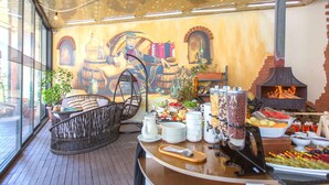 A breakfast buffet with a variety of food options, a brick oven, wicker furniture, and a mural on the wall. - Cron Palace Tbilisi Hotel (Tbilisi)