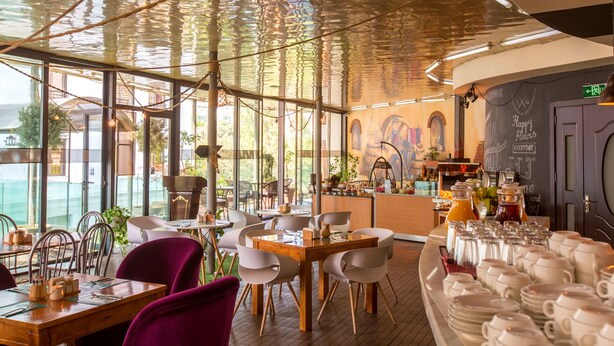 A restaurant with a high ceiling, large windows, and a bar area. - Cron Palace Tbilisi Hotel (Tbilisi)