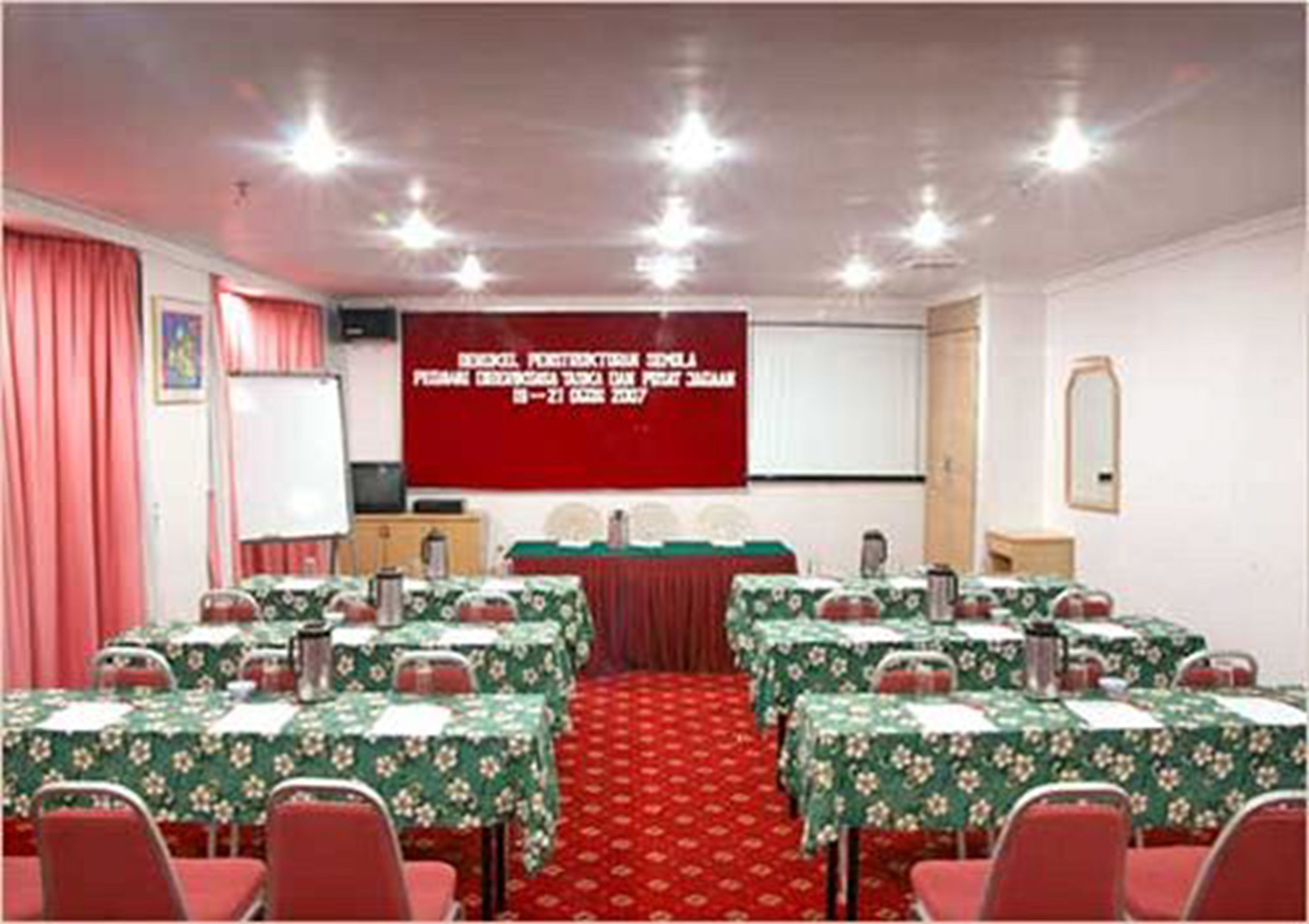 A conference room with tables set for a meeting, a projector screen, and a red carpeted floor.