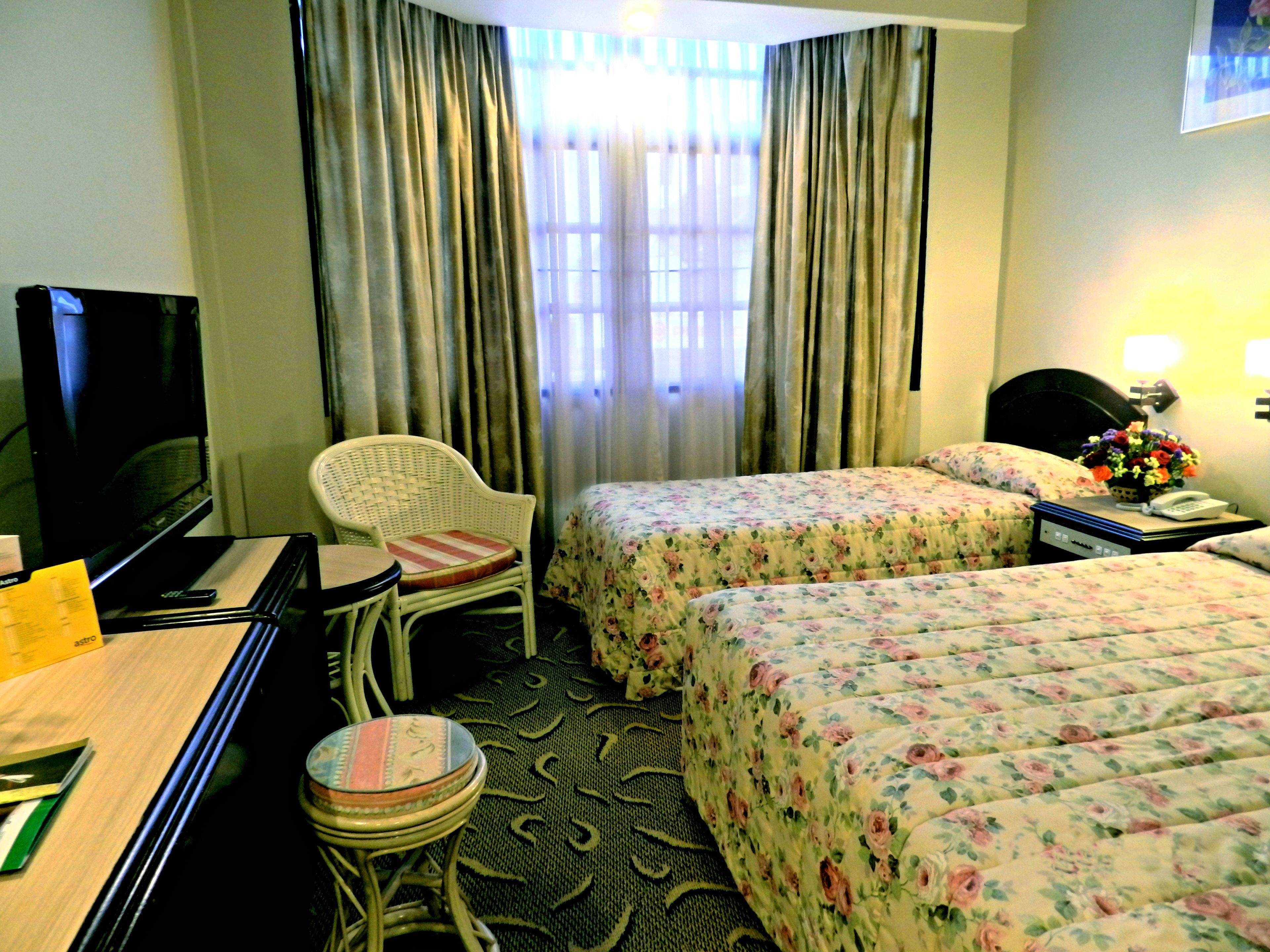 A hotel room with two beds, a desk, a chair, a television, and a telephone.