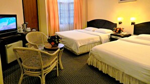 Habitación de hotel con dos camas, televisor, una silla y un escritorio con un jarrón de flores.