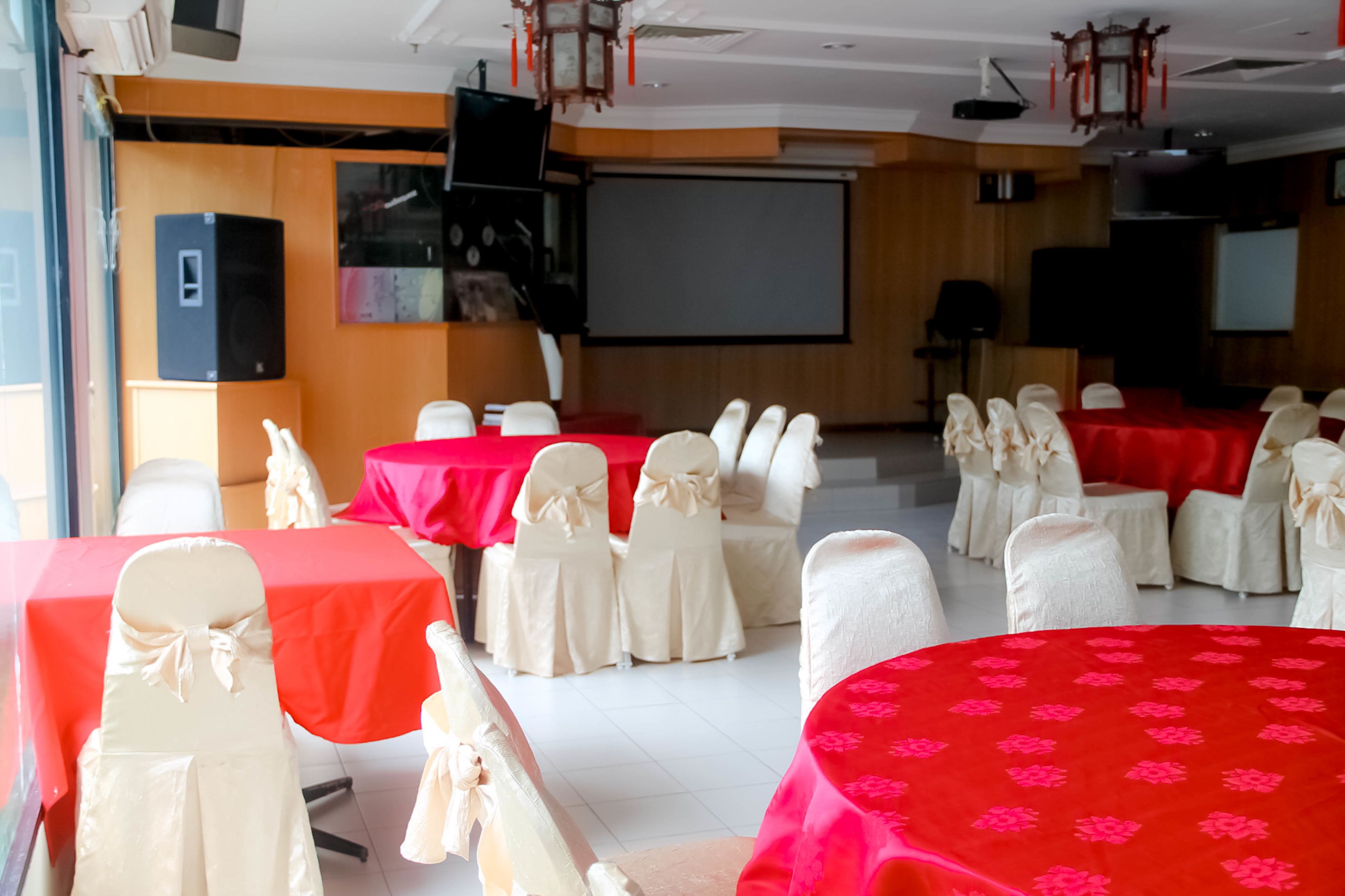 Una sala conferenze con diversi tavoli ricoperti da tovaglie rosse e sedie bianche decorate con nastri bianchi.