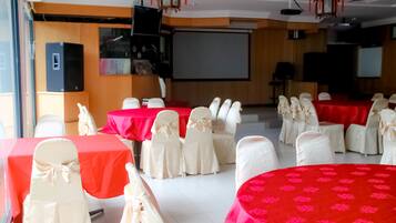 Una sala conferenze con diversi tavoli ricoperti da tovaglie rosse e sedie bianche decorate con nastri bianchi.